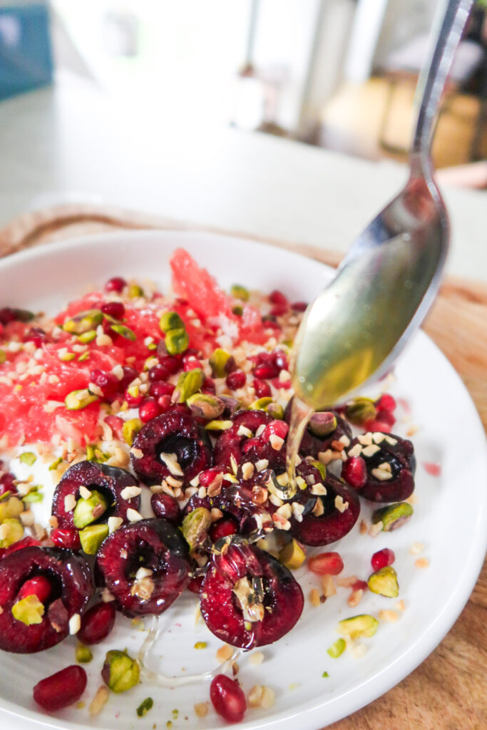 Assembled breakfast bowl with red grapefruit, cherries, and a drizzle of honey on thick yoghurt