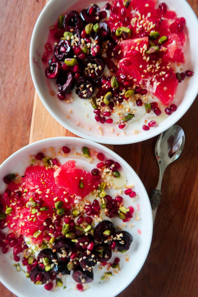 Overhead shot of a breakfast bowl with yoghurt, cherries, grapefruit, and pistachios layered in a ceramic dish