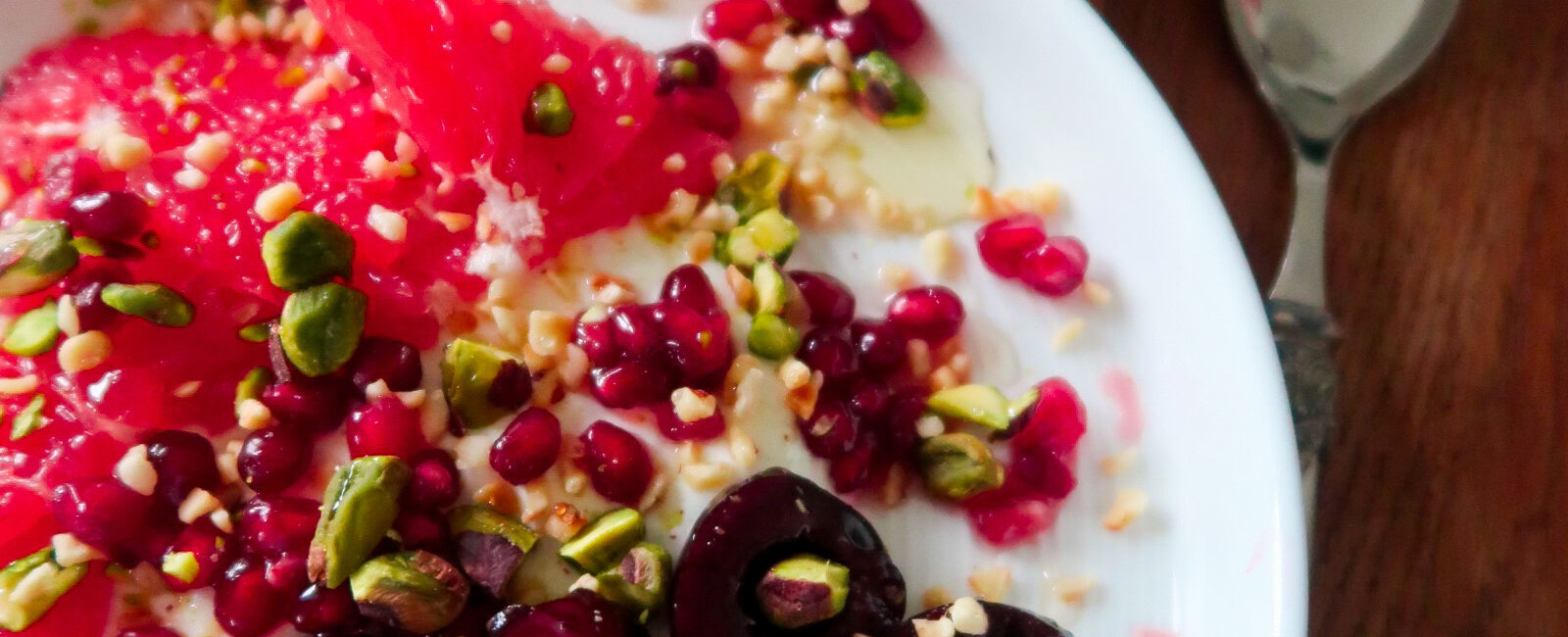 Overhead shot of a breakfast bowl with yoghurt, cherries, grapefruit, and pistachios layered in a ceramic dish
