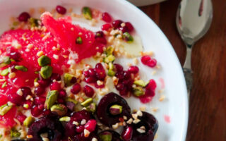 Overhead shot of a breakfast bowl with yoghurt, cherries, grapefruit, and pistachios layered in a ceramic dish