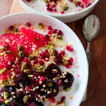 Overhead shot of a breakfast bowl with yoghurt, cherries, grapefruit, and pistachios layered in a ceramic dish