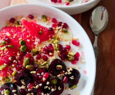 Overhead shot of a breakfast bowl with yoghurt, cherries, grapefruit, and pistachios layered in a ceramic dish