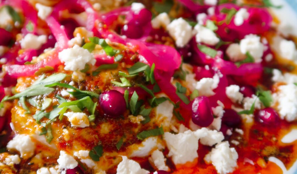 Bowl of Turkish eggs topped with spiced butter, pomegranate, feta and herbs