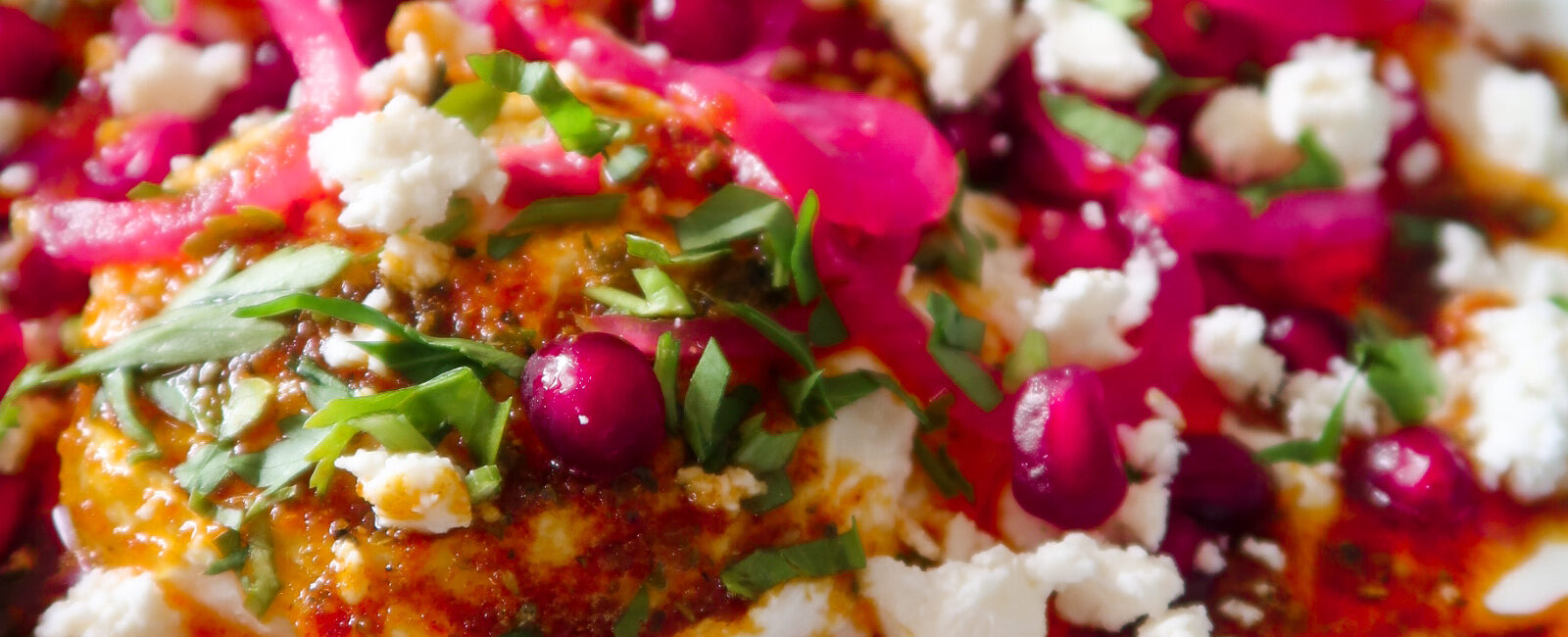 Bowl of Turkish eggs topped with spiced butter, pomegranate, feta and herbs