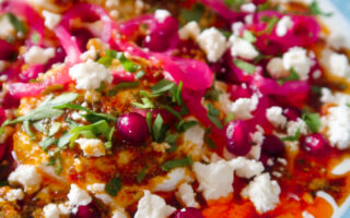 Bowl of Turkish eggs topped with spiced butter, pomegranate, feta and herbs