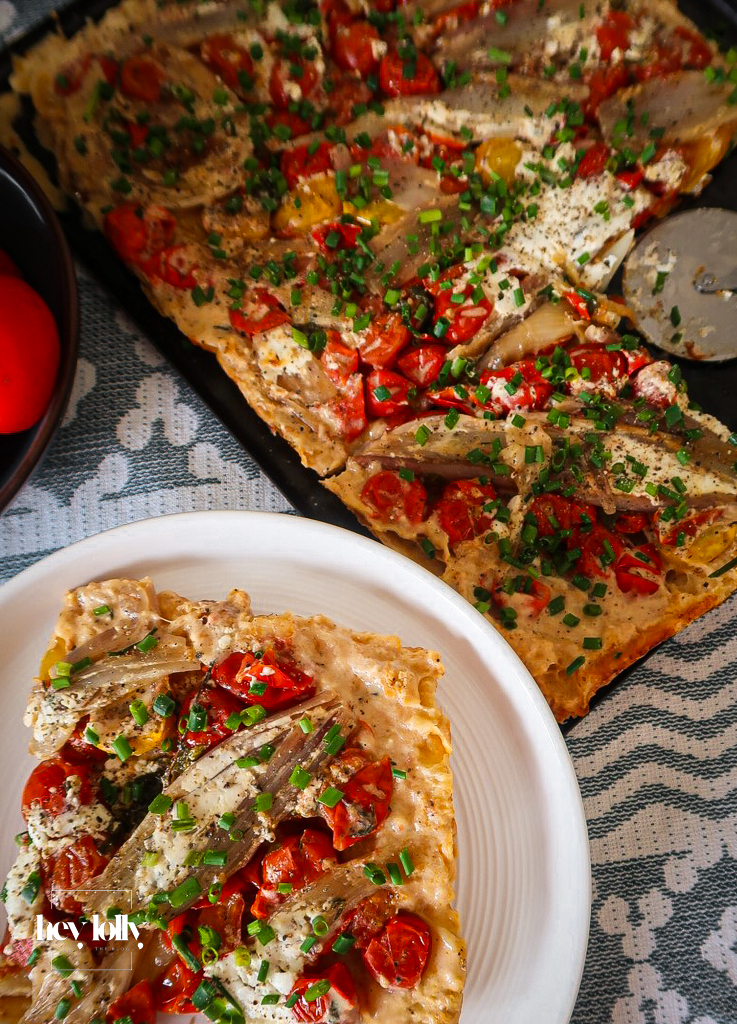 Golden shallot and tomato tart topped with fresh basil leaves on a white plate