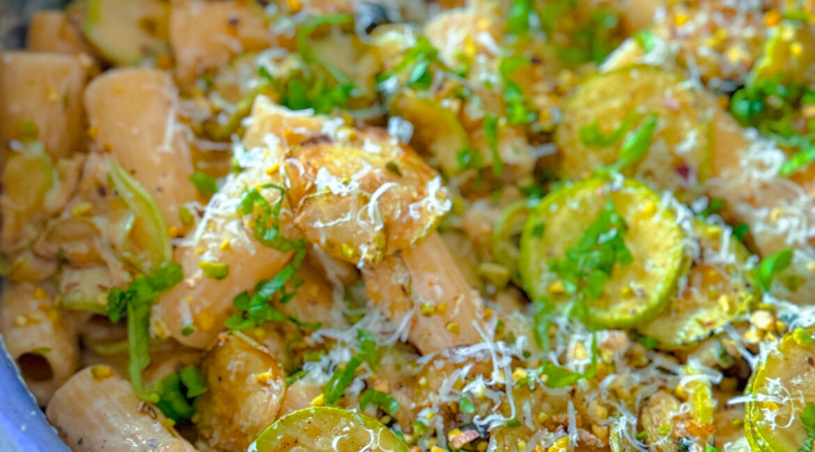 Bowl of courgette lemon ricotta rigatoni topped with torn basil, pine nuts and lemon zest.