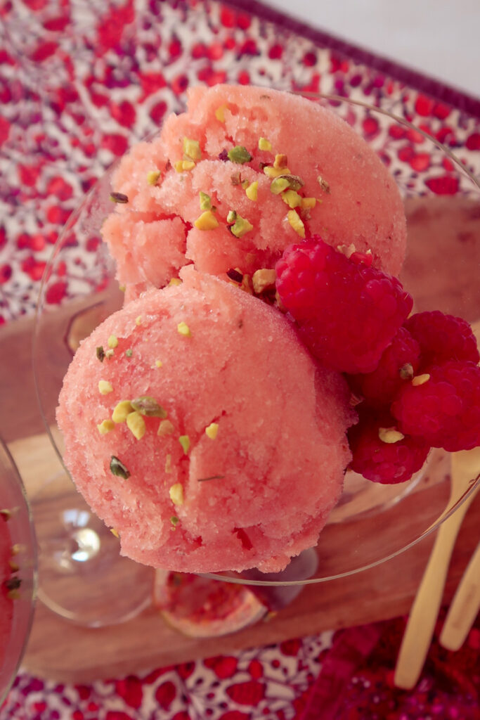 Scoops of nectarine and passion fruit sorbet in chilled glass with pistachio garnish