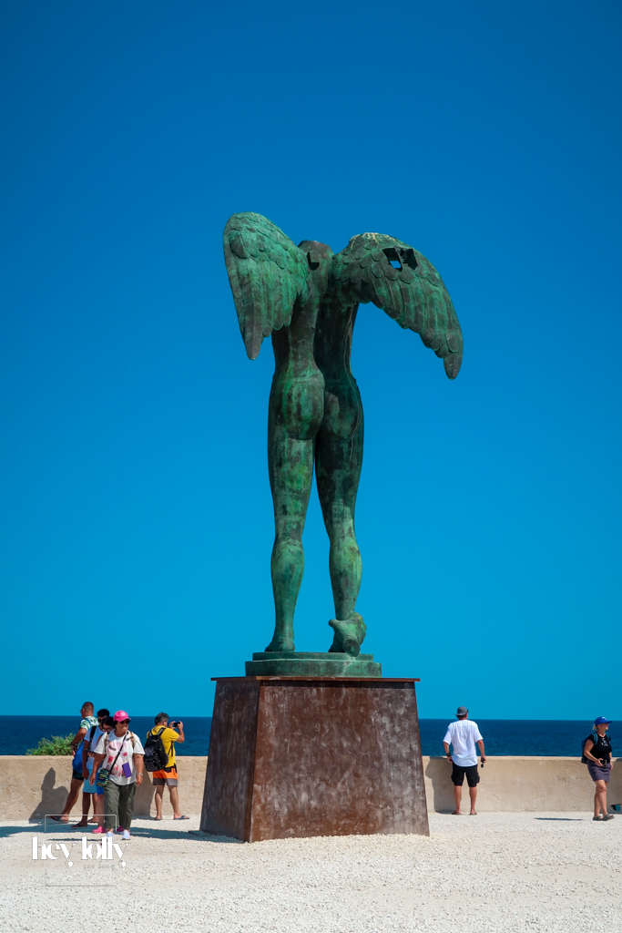 Monumental bronze statue of Ikaria with wings against the sea in Ortigia
