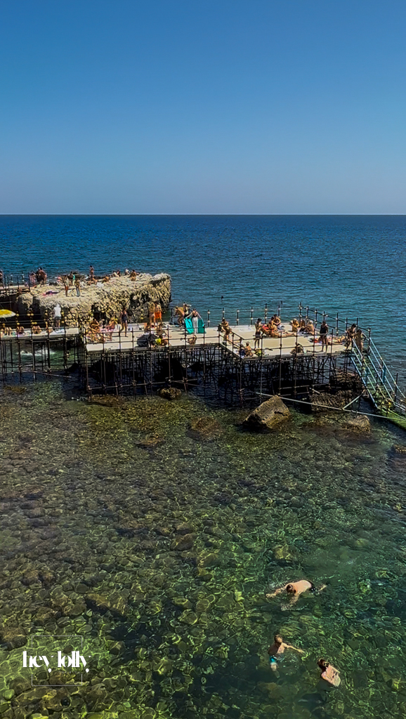 Wooden sunbathing platform with swimmers diving into clear turquoise waters in Ortigia