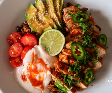 Chicken burrito bowl topped with sliced chicken, avocado, beans, sweetcorn, cheddar, and chilli cream drizzle.