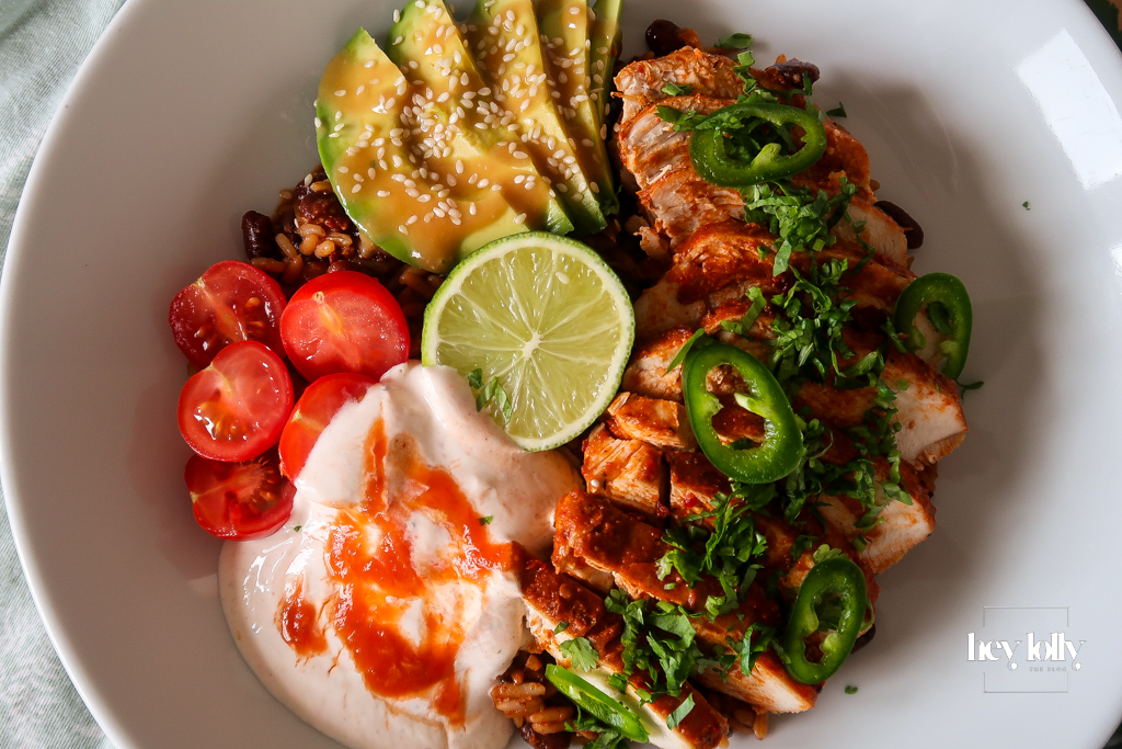 Chicken burrito bowl topped with sliced chicken, avocado, beans, sweetcorn, cheddar, and chilli cream drizzle.