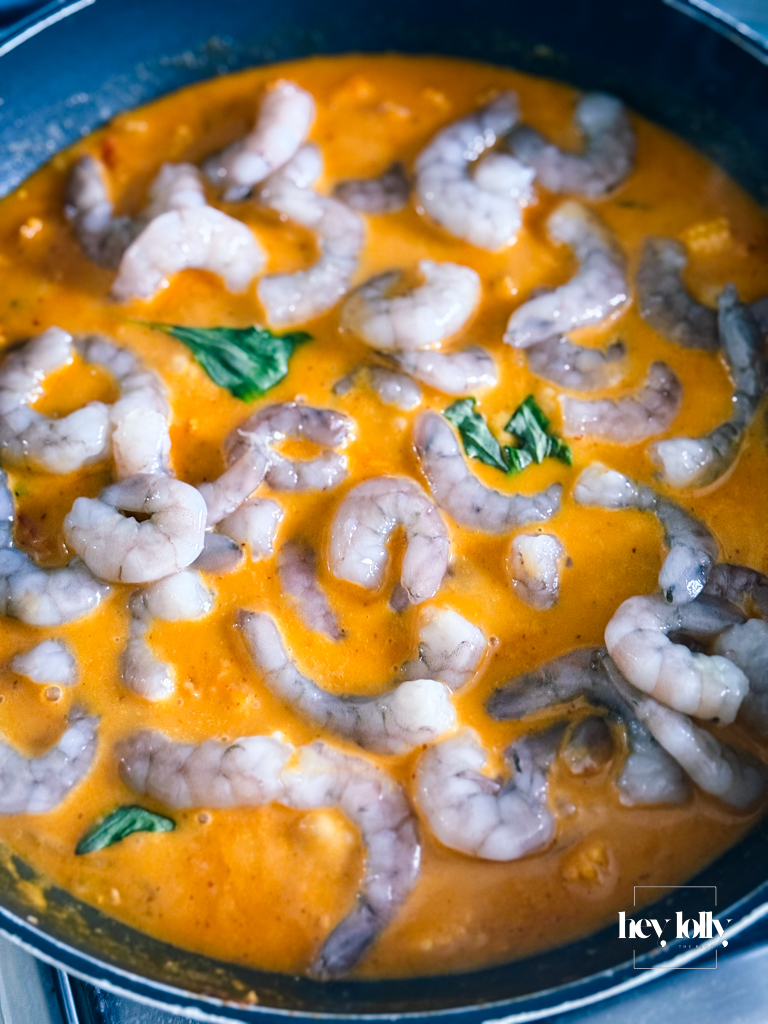 Raw prawns added to bubbling red curry sauce before cooking through.