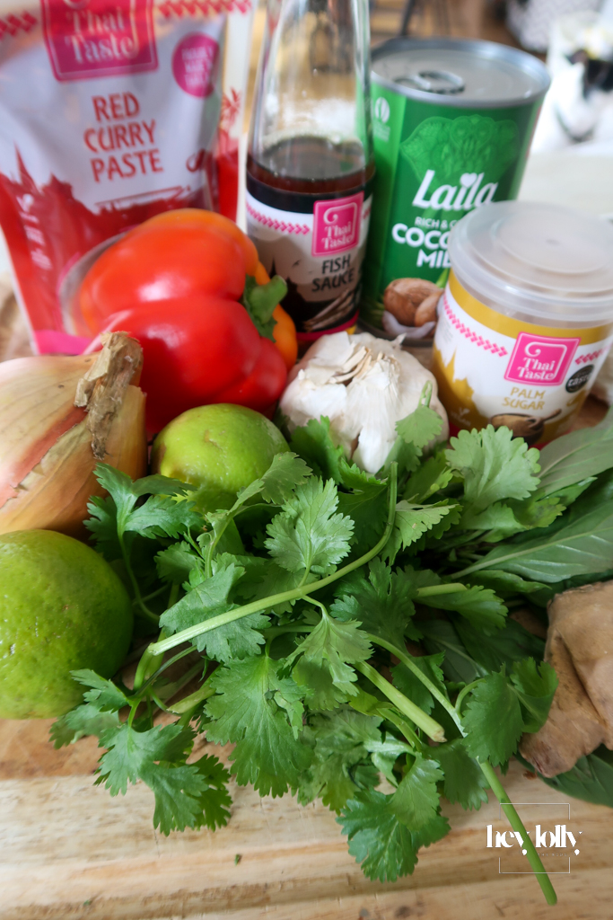 Overhead shot of fresh ingredients for Thai Red King Prawn curry including prawns, baby corn, red pepper, and courgette on a wooden board.
