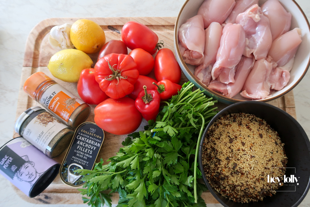 Flat lay of ingredients for Za’atar Chicken Thighs recipe including chicken thighs, za’atar, cumin, tomatoes, and anchovies