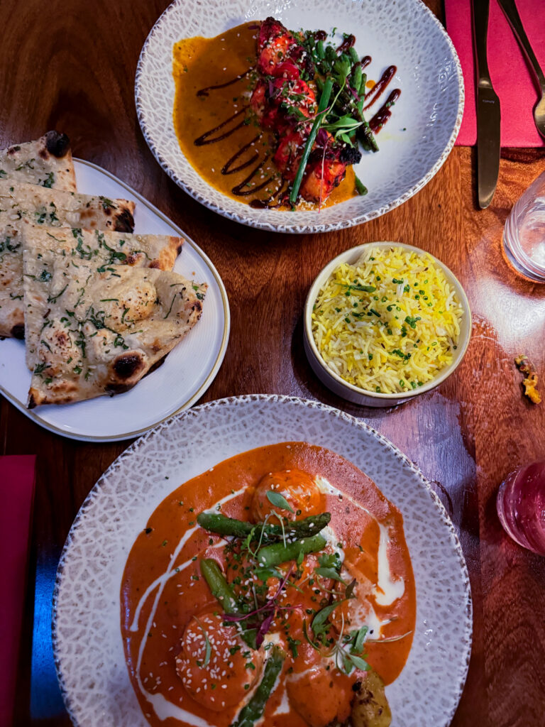 Overhead shot of mains at Passan’s Nottingham — Tandoori Monkfish, Malai Chicken, Garlic Naan, and Pilau Rice served on a dark wooden table.