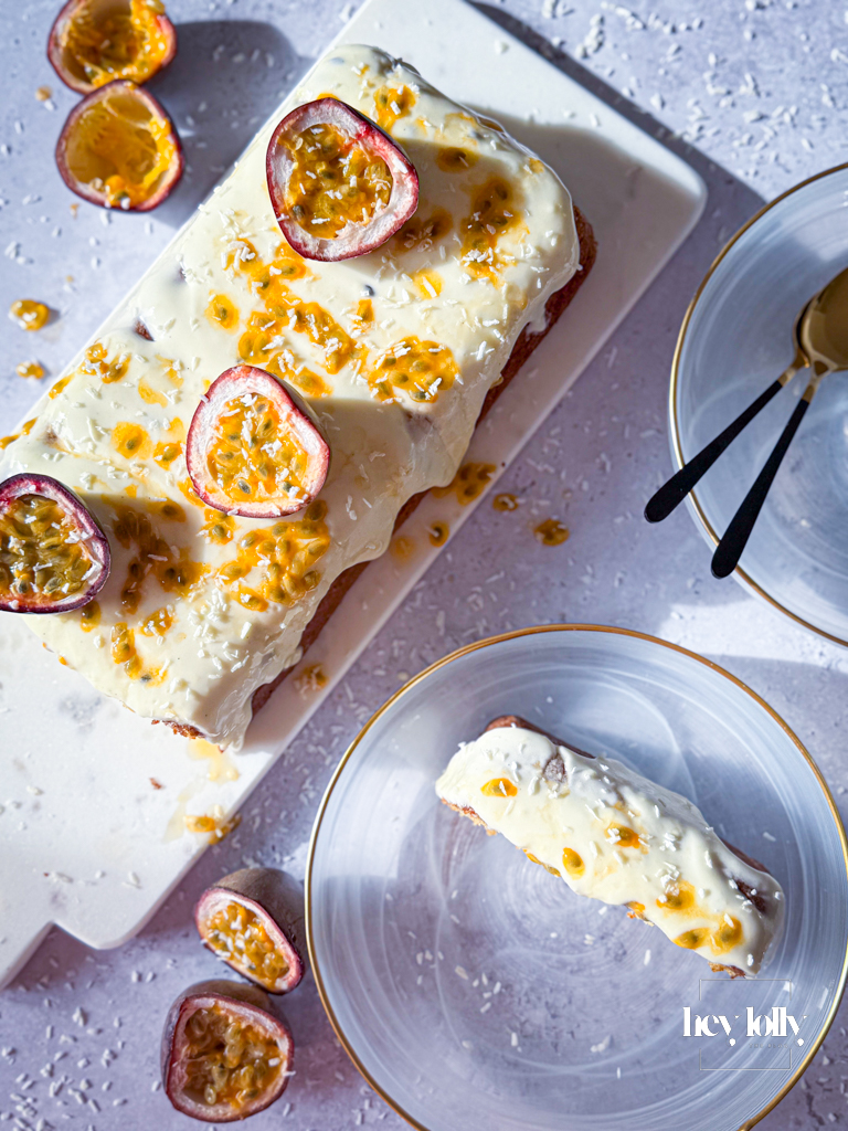 Finished passion fruit yoghurt loaf with cream cheese frosting and glossy passion fruit drizzle, golden and vibrant on white plate.