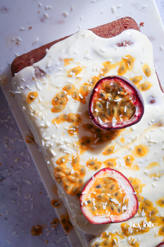 Hand holding slice of passion fruit yoghurt loaf with frosting glistening under natural light.