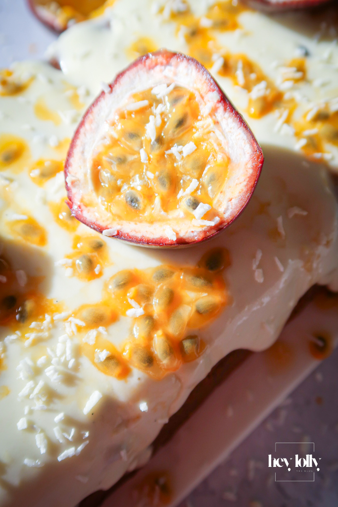 Finished passion fruit yoghurt loaf with cream cheese frosting and glossy passion fruit drizzle, golden and vibrant on white plate.