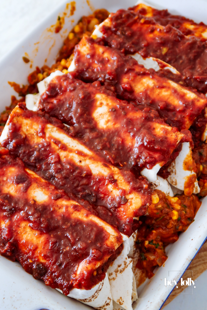 Assembled enchiladas in a baking dish covered with chipotle tomato sauce and grated cheese before baking.