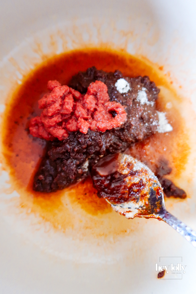 Garlic and chipotle paste bubbling in tomato sauce on the hob — rich red colour and steam rising.