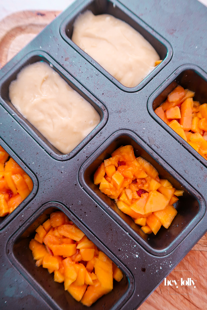 Thick yoghurt-olive-oil batter being spooned over fig and papaya in a muffin tin