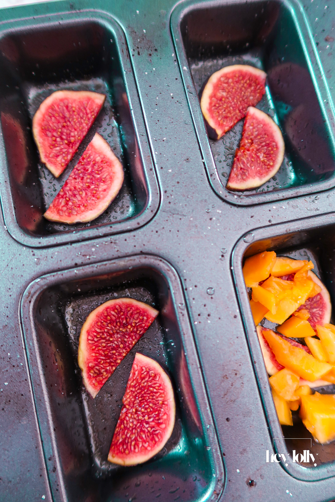 Muffin tin lined with fig slices and diced papaya ready for upside-down cakes