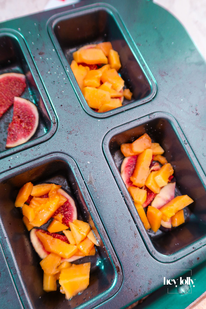Muffin tin lined with fig slices and diced papaya ready for upside-down cakes