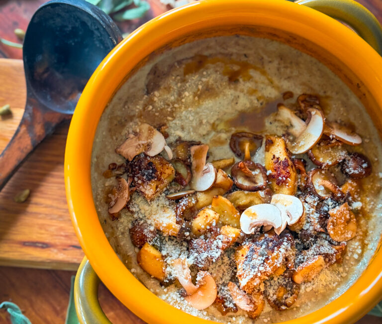 Close-up bowl of creamy mushroom gnocchi soup with bronze mushrooms, thyme and parmesan shavings, steam rising on a rustic table.