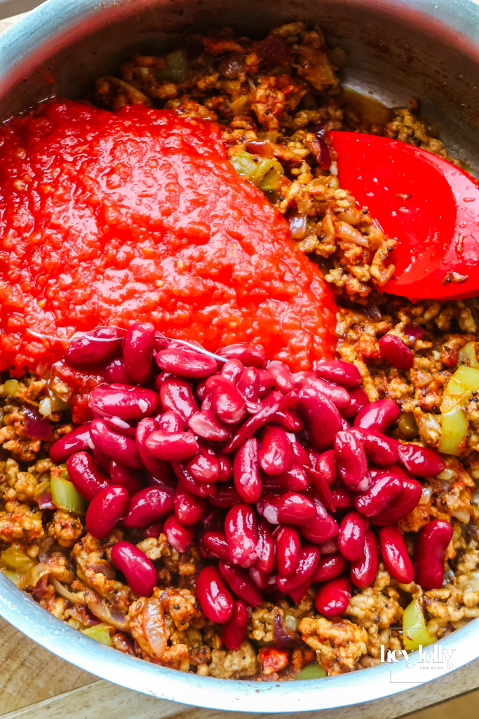 Kidney beans being stirred through the simmering chicken keema in the pan