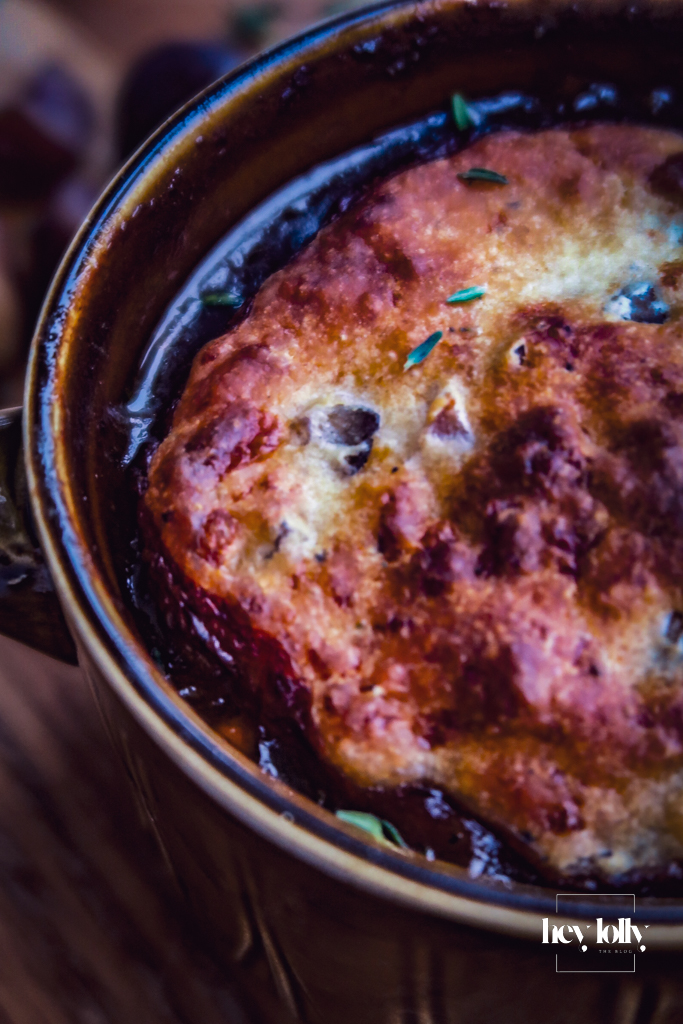Overhead shot of herby chestnut and cheddar beef cobbler on a wooden table, golden beef cobbler ready to serve.
