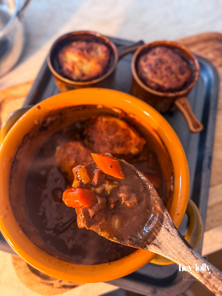 Spoon lifting a portion of beef cobbler from the dish, showing tender beef and cheesy cobble topping.