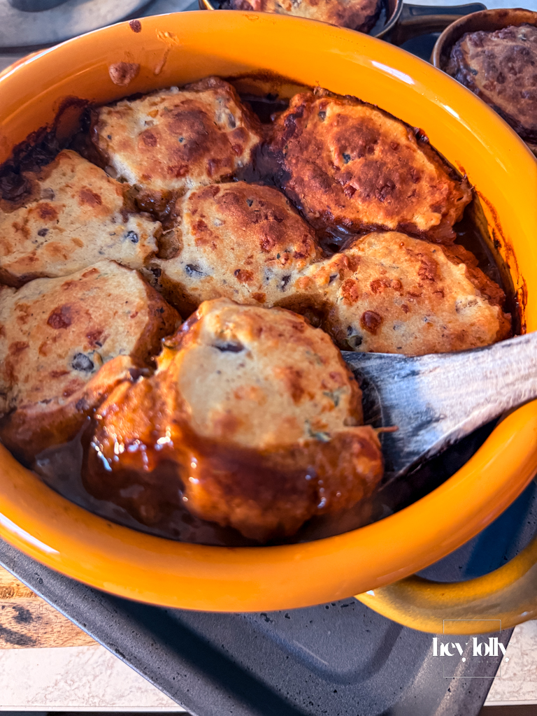 Spoon lifting a portion of beef cobbler from the dish, showing tender beef and cheesy cobble topping.