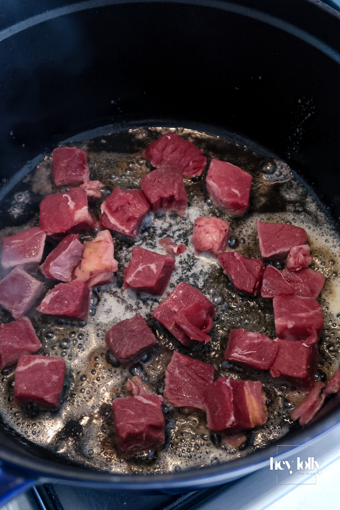 Chunks of braising beef browning in a heavy casserole dish for beef cobbler, edges seared and caramelised.