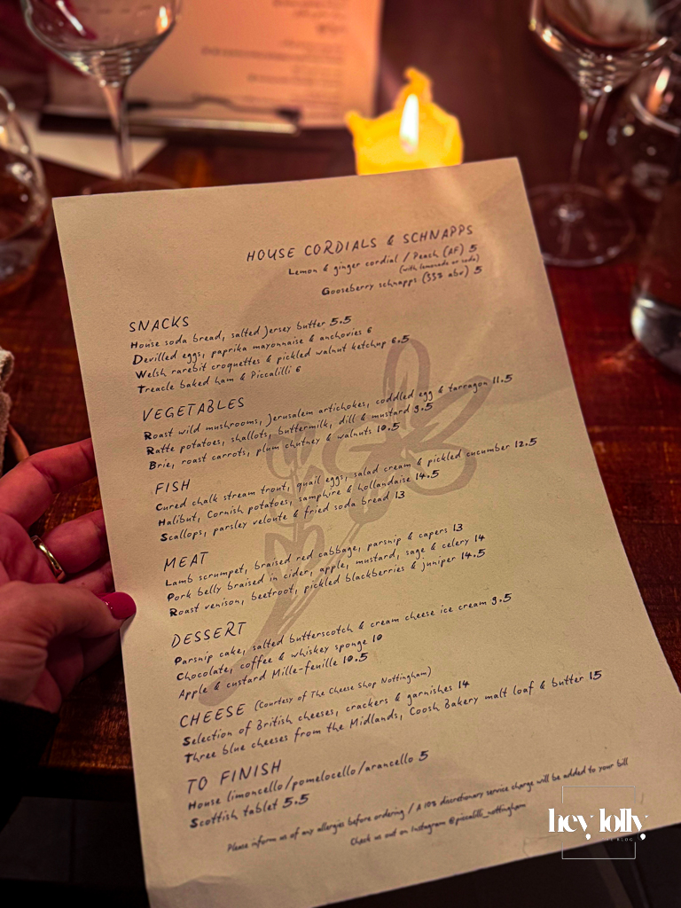 Handwritten Piccalilli Nottingham menu held over a candlelit wooden table with wine glasses