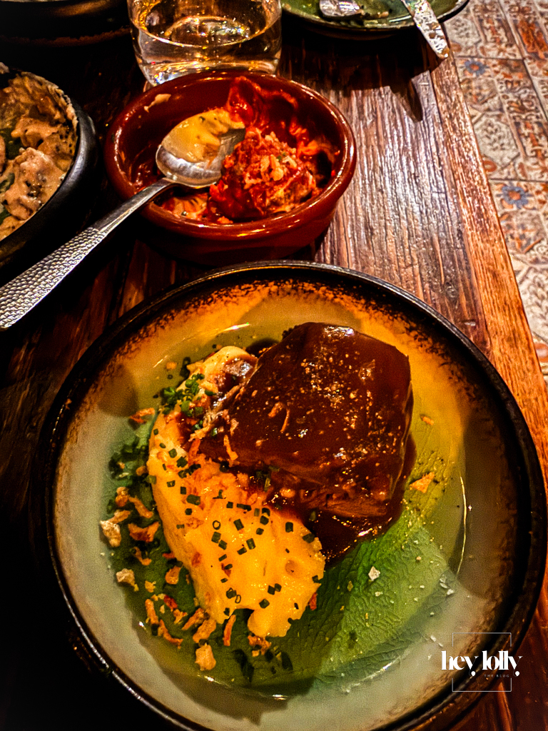 Carne estofada at Plates by Purnell’s – braised beef with mashed potato, gravy and chives in a deep green bowl on a wooden table.