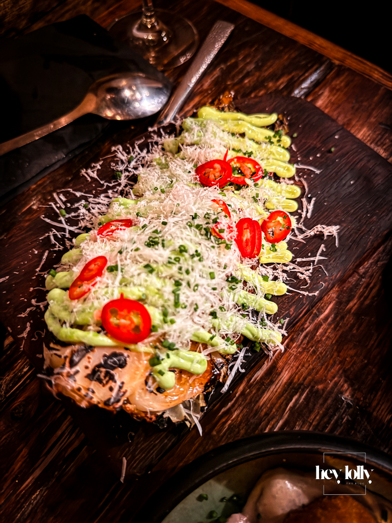 Repollo con harissa y queso at Plates by Purnell’s – grilled cabbage on a wooden board, smothered in green sauce, grated cheese and sliced red chilli.