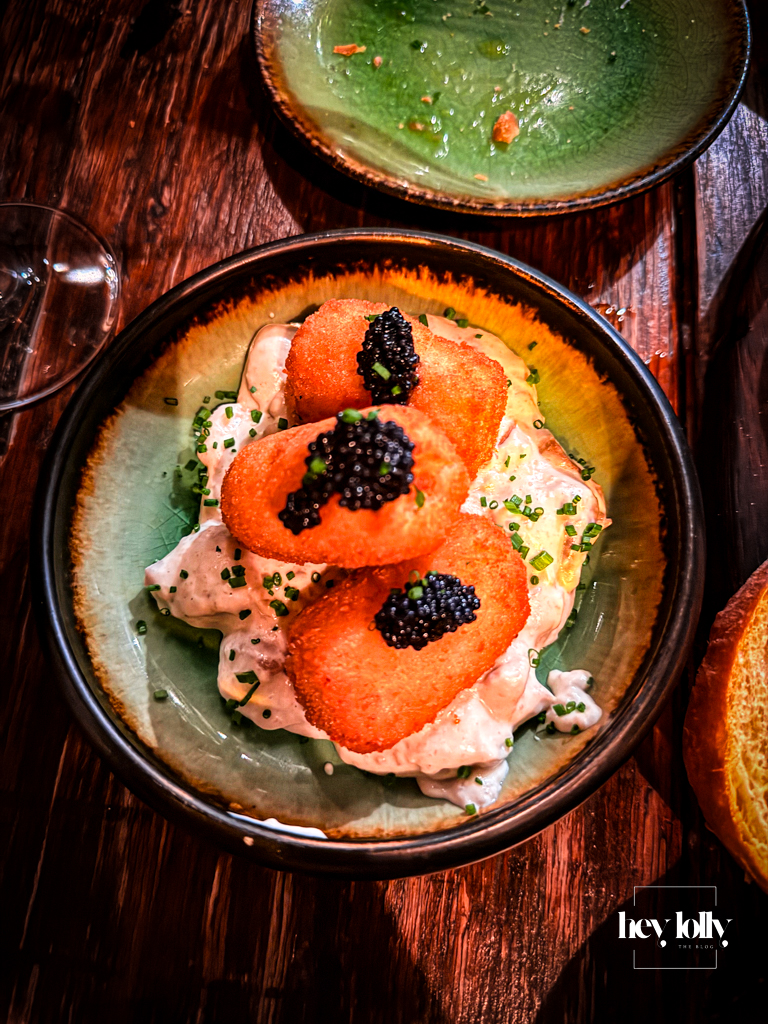 Croquetas de bacalao at Plates by Purnell’s – stacked salt cod croquettes topped with black roe, sitting on a creamy salad on a green ceramic plate