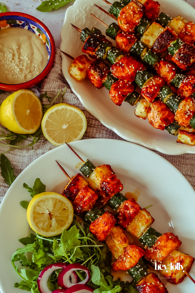 Salmon, Courgette & Halloumi Skewers with Lemon Tahini Dressing, topped with herbs and lemon wedges.