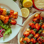 Salmon, Courgette & Halloumi Skewers with Lemon Tahini Dressing, topped with herbs and lemon wedges.
