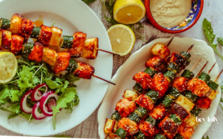 Salmon, Courgette & Halloumi Skewers with Lemon Tahini Dressing, topped with herbs and lemon wedges.