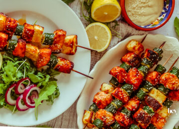 Salmon, Courgette & Halloumi Skewers with Lemon Tahini Dressing, topped with herbs and lemon wedges.