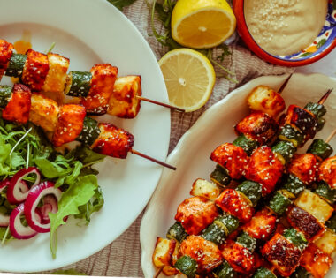 Salmon, Courgette & Halloumi Skewers with Lemon Tahini Dressing, topped with herbs and lemon wedges.