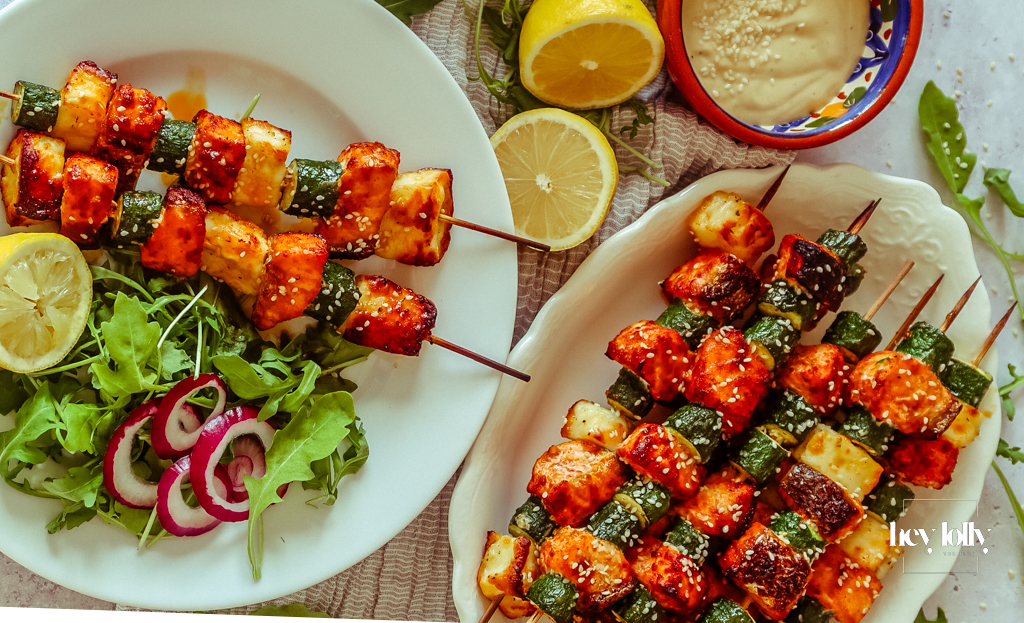 Salmon, Courgette & Halloumi Skewers with Lemon Tahini Dressing, topped with herbs and lemon wedges.