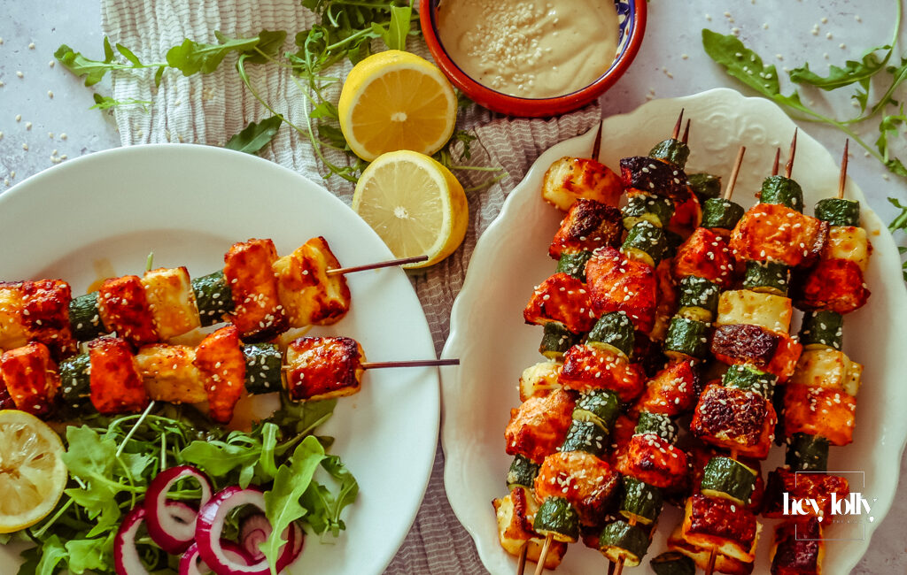 Salmon, Courgette & Halloumi Skewers with Lemon Tahini Dressing, topped with herbs and lemon wedges.