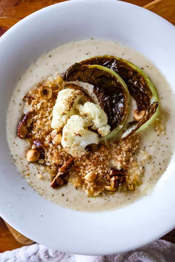 Overhead shot of cauliflower and white bean soup with toasted chopped nuts and roasted cauliflower ends.