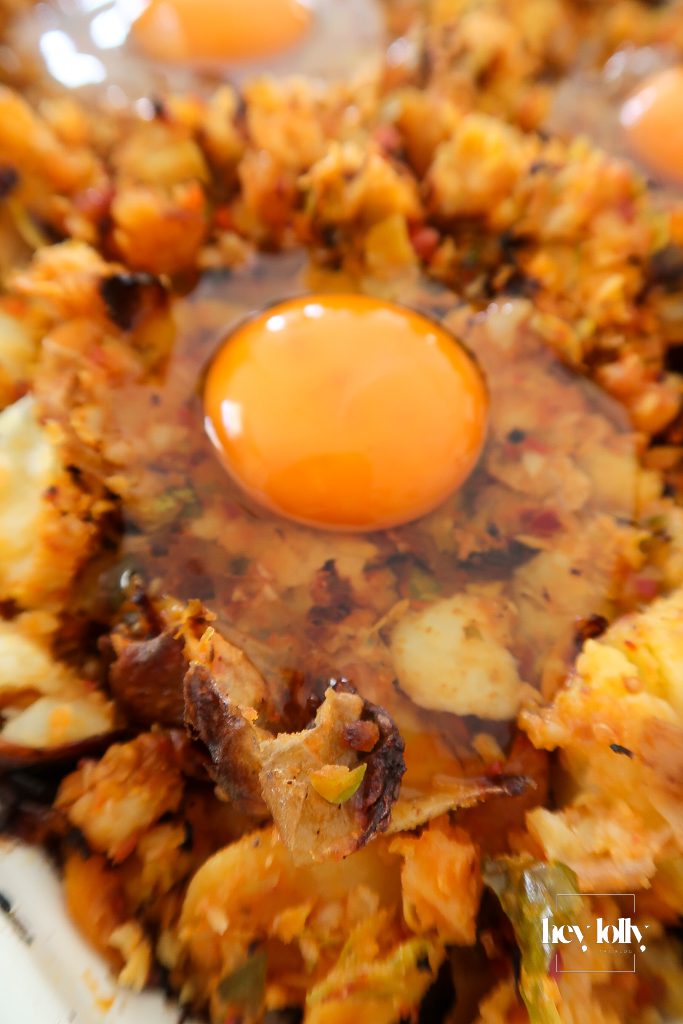 Sunny-side eggs cracked into sprout and harissa potato hash while cooking