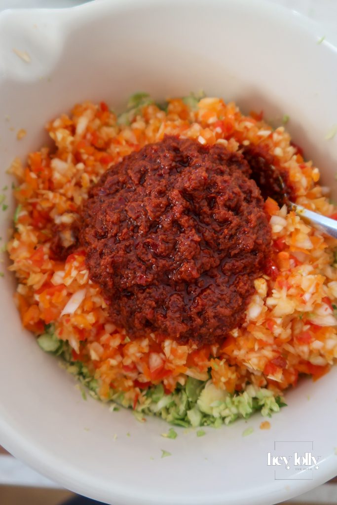 Harissa being stirred through potatoes and sprouts for a spiced breakfast hash