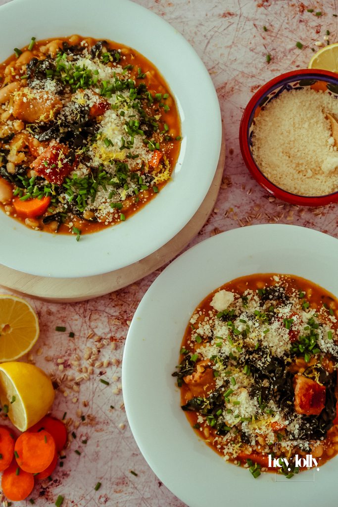 Overhead shot of pearl barley stew with smoky sausages, roast carrots, white beans and kale in a rustic bowl