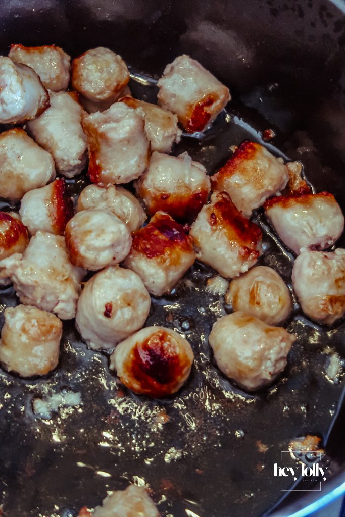 Sausages browning in a heavy-bottomed pot as the first step of pearl barley stew